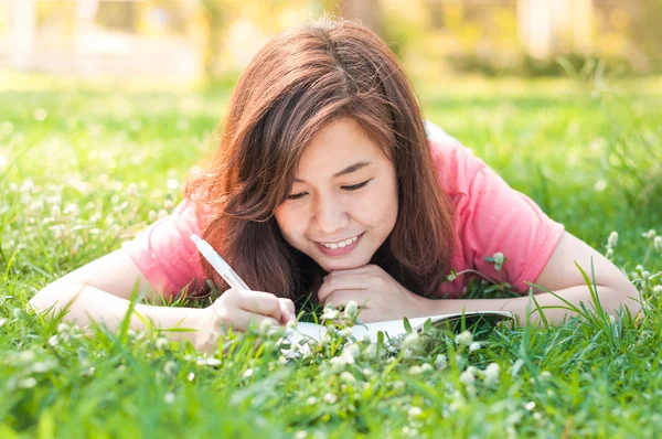 Glad ung asiatisk kvinna skriver i anteckningsboken och ler — Stockfoto