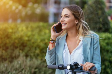 İş kadını elektrikli scooterla akıllı telefondan konuşuyor.