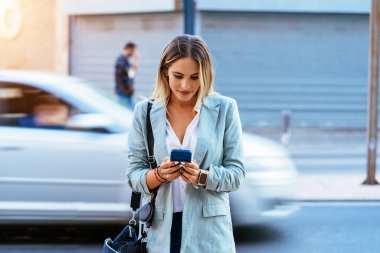 Şehir caddesinde akıllı telefonlara bakan moda bir kadın