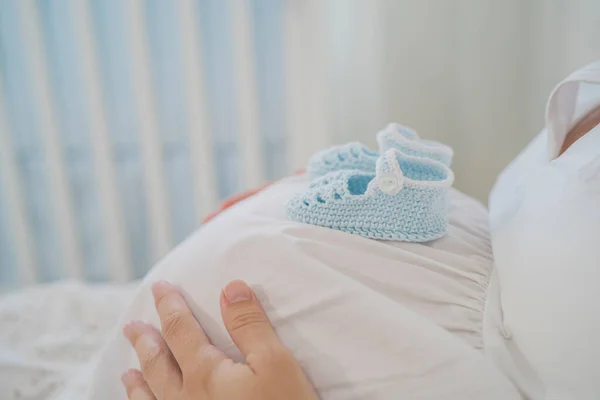 Ernte gesichtslose schwangere Dame mit Babyschuhen auf Bauch auf dem Bett liegend — Stockfoto