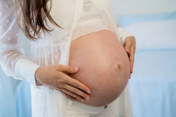 Анонимная беременная женщина касается живота в светлой комнате — стоковое фото