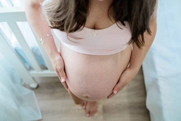 Безликая босиком беременная женщина гладит живот в спальне — стоковое фото