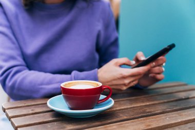 Kesici kadın akıllı telefon kullanıyor ve kahve içiyor.
