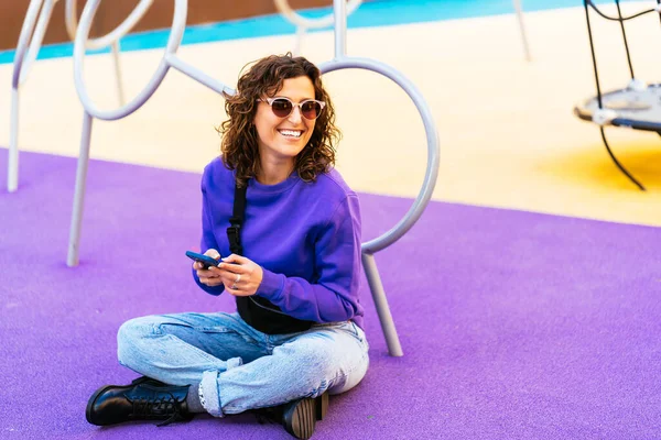 Akıllı telefonlu neşeli öğrenci yerde oturuyor.