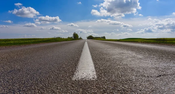 Bulutlu mavi gökyüzünün altında açık kırsal alanda ortaya odaklanan katranlı yolun düşük açılı görüntüsü