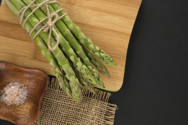 Kesme tahtasında bir sürü taze kuşkonmaz siyah arka planda fotokopi alanı yukarıdan aşağıya doğru görünüyor. Kuşkonmaz pişirme konsepti