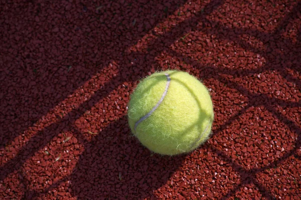 Shadows of net surrounding a tennis ball on outdoor court in sunshine, sport and active lifestyle concept