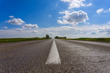 Bulutlu mavi gökyüzünün altında açık kırsal alanda ortaya odaklanan katranlı yolun düşük açılı görüntüsü