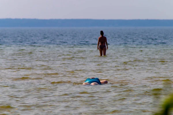 Mayo giymiş şişman bir kadın suyun içinde yatıyor. Göl sahilinde tatil..