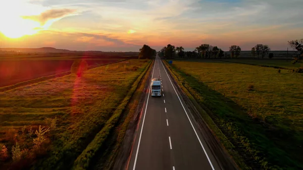 İnanılmaz Hava Aracı Görünümü: Beyaz Kamyon Yoldan Mal Teslim Ediyor. Sunset Summer saati: Blue Sky, Red Sun. Güneş ışınları yolu aydınlatıyor..
