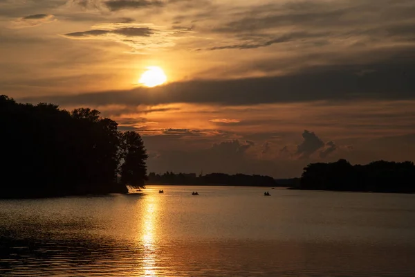 Sunset 'teki gölün üstünde efsanevi kırmızı bulutlar. Şehir parkında teknelerle gezen insanlar..