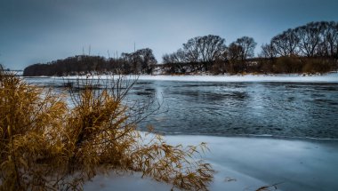 Kış manzarası, kıyılar boyunca donmuş bir nehir ve bitki örtüsü.
