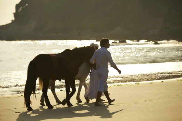 A couple walking horses on beach — Stock Photo, Image