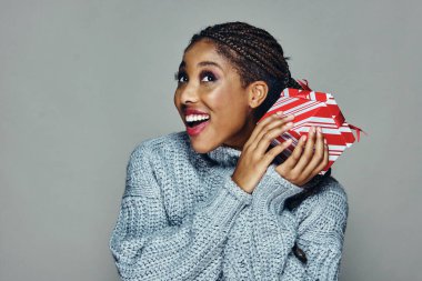 Şaşırmış güzel bir kadın, gri arka planda Noel hediyesini sallarken yukarı bakıyor.