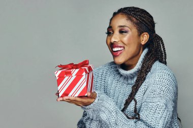 Siyah örgülü saçları olan mutlu genç bir kadın gri arka planda Xmas 'a hediye veriyor.
