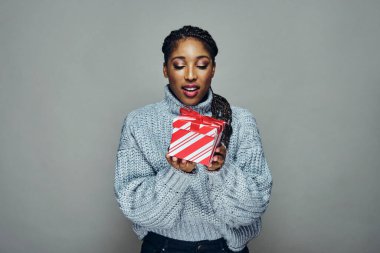 Çizgili kırmızı Xmas hediyesine bakan hırkalı çekici genç bir kadın.