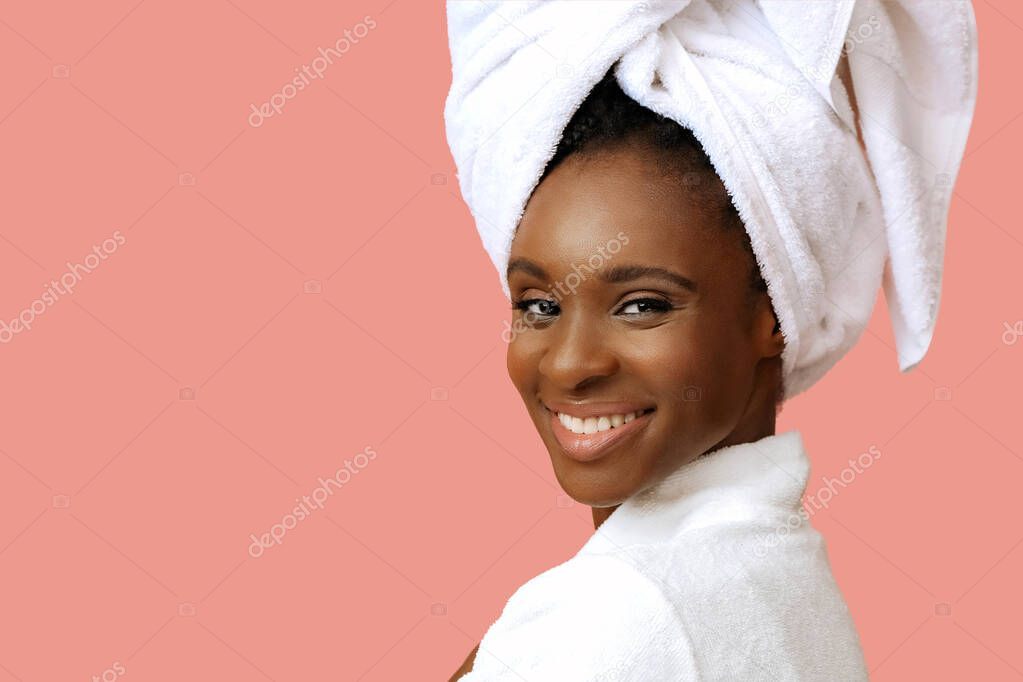 Young beautiful woman in bathrobe with white towel on head posing on pink background