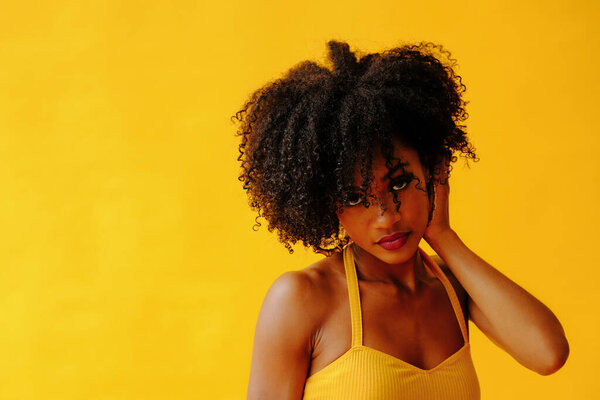 Beautiful young African american woman in bright summer outfit posing isolated on yellow background