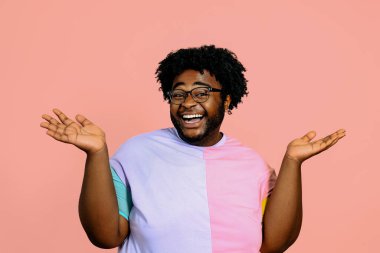 Genç mutlu Afrikalı Amerikalı adam stüdyoda pembe arka planda poz veriyor. 