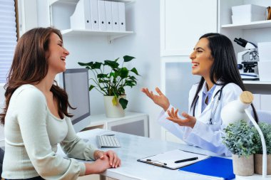 Kadın doktor ve bayan hasta tıp merkezinde masada otururken bir şey tartışıyorlar. 