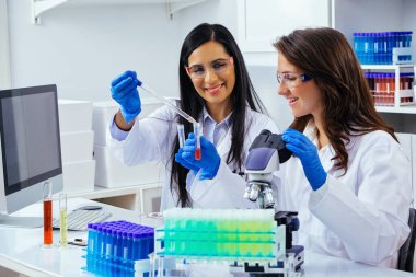 Laboratuvarda deney tüpleri ve mikroskop ile çalışan iki güzel bayan bilim adamı araştırma yapıyor. 