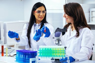 Laboratuvarda deney tüpleriyle çalışan iki güzel genç bilim kadını araştırma yapıyor. 