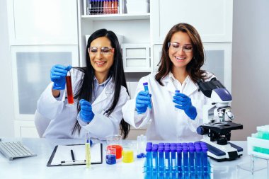 Laboratuvarda deney tüpleriyle çalışan iki güzel genç bilim kadını araştırma yapıyor. 