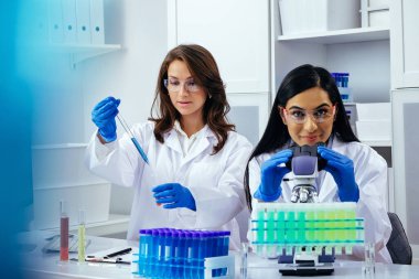 Laboratuvarda deney tüpleri ve mikroskop ile çalışan iki güzel bayan bilim adamı araştırma yapıyor. 