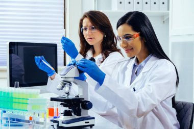 Laboratuvarda deney tüpleri ve mikroskop ile çalışan iki güzel bayan bilim adamı araştırma yapıyor. 