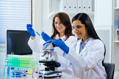 Laboratuvarda deney tüpleri ve mikroskop ile çalışan iki güzel bayan bilim adamı araştırma yapıyor. 