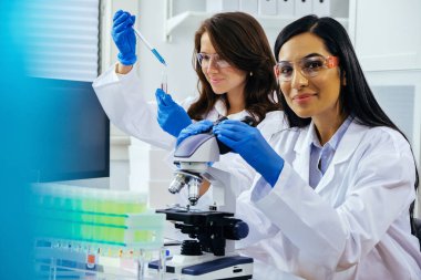 Laboratuvarda deney tüpleri ve mikroskop ile çalışan iki güzel bayan bilim adamı araştırma yapıyor. 