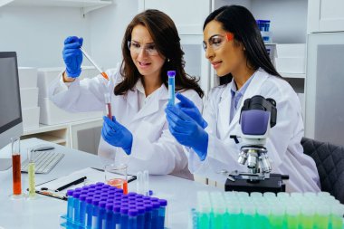 Laboratuvarda deney tüpleriyle çalışan iki güzel genç bilim kadını araştırma yapıyor. 