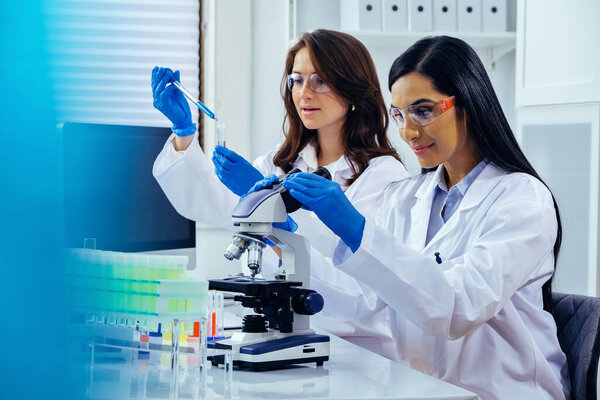 Two beautiful young female scientists working in laboratory with test tubes and microscope doing some research 