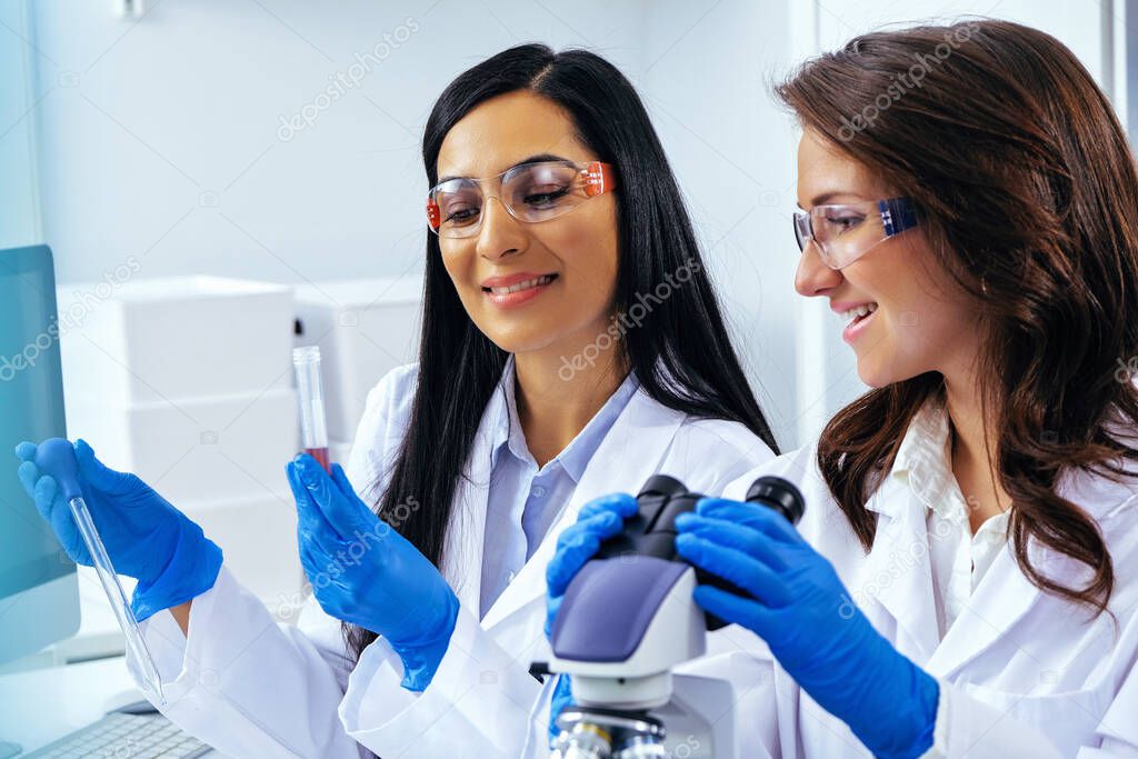 Two beautiful young female scientists working in laboratory with test tubes and microscope doing some research 