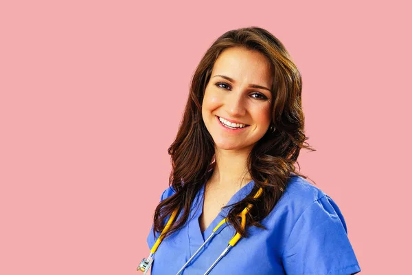 クローズアップポートレートの笑顔女性医師または看護師とともにStethoscopeで青制服上のピンクのスタジオの背景 — ストック写真