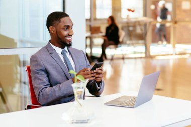 Ofisinde cep telefonu ve dizüstü bilgisayarı olan Afro-Amerikan iş adamı
