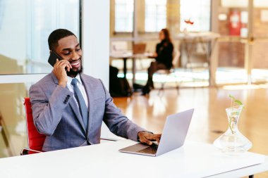 Genç Afrikalı Amerikalı iş adamı ofiste masada otururken telefonla konuşuyor.