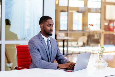Afro-Amerikan iş adamı masada oturuyor ve dizüstü bilgisayarla çalışıyor.