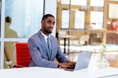 Afro-Amerikan iş adamı masada oturuyor ve dizüstü bilgisayarla çalışıyor.
