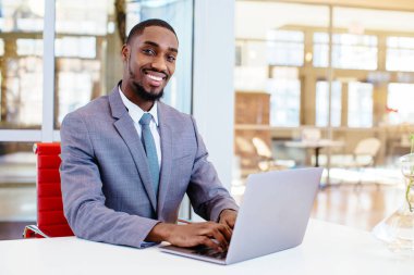 Masada oturup kameraya bakan gülümseyen Afro-Amerikan bir iş adamının portresi.