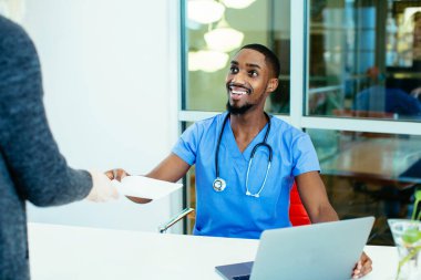 Steteskop ve dizüstü bilgisayarı olan Afro-Amerikan doktor ofiste kadın hastayla konuşuyor..