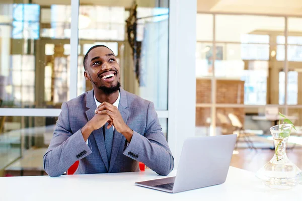 Genç, gülümseyen Afrikalı Amerikalı iş adamı masada oturuyor ve başka tarafa bakıyor. 