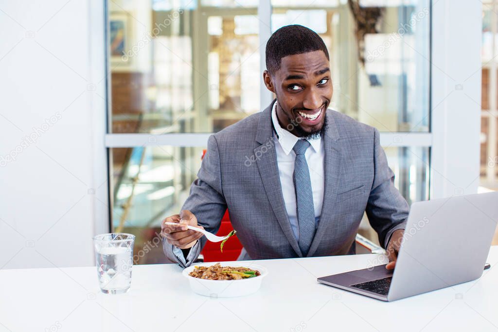 african american businessman eating while working on laptop in office 