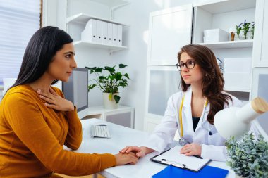 Genç bayan doktor klinikte hastasıyla konuşuyor.