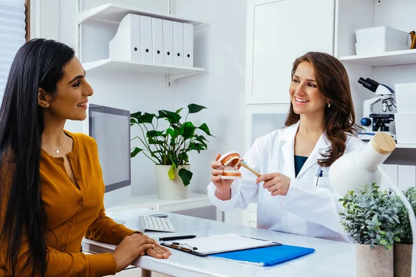 Gülümseyen kadın doktor kadın hastaya insan çenesi ve diş modeli gösteriyor 