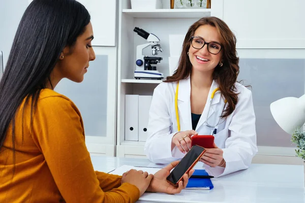 Kadın doktor ve hasta hastanede cep telefonu kullanıyor.