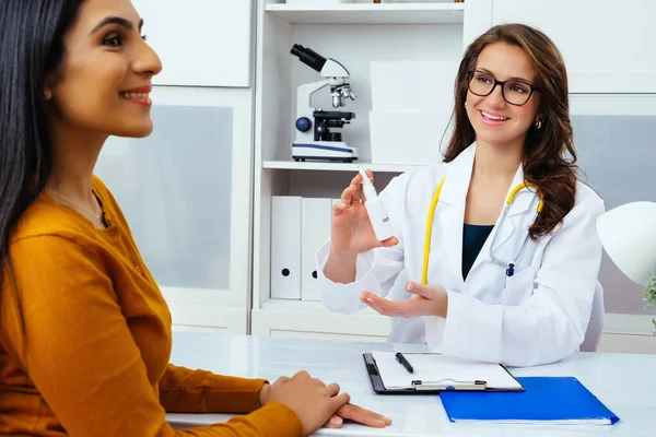 Gülümseyen kadın doktor kadın hastasına burun spreyi gösteriyor. 