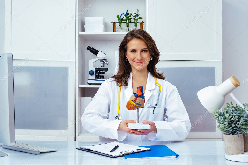 beautiful smiling female doctor showing human heart mockup in office