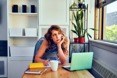 Dizüstü bilgisayarı ve kahvesi olan genç bir kız öğrenci evde ders çalışıyor.