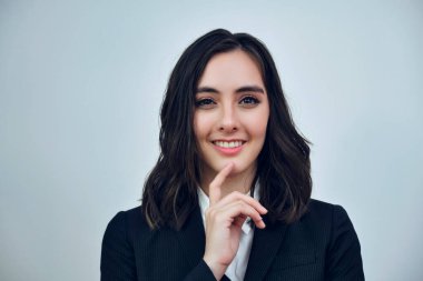 Beyaz arka planda siyah ceket giyen gülümseyen genç bir iş kadınının portresi.